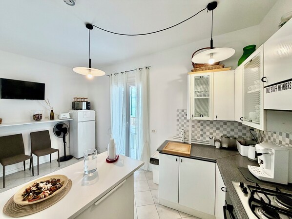 A modern kitchen with a central island, white cabinetry, a microwave, a refrigerator, and a gas stove. - Ma&Mi Guest House (Cefalù)