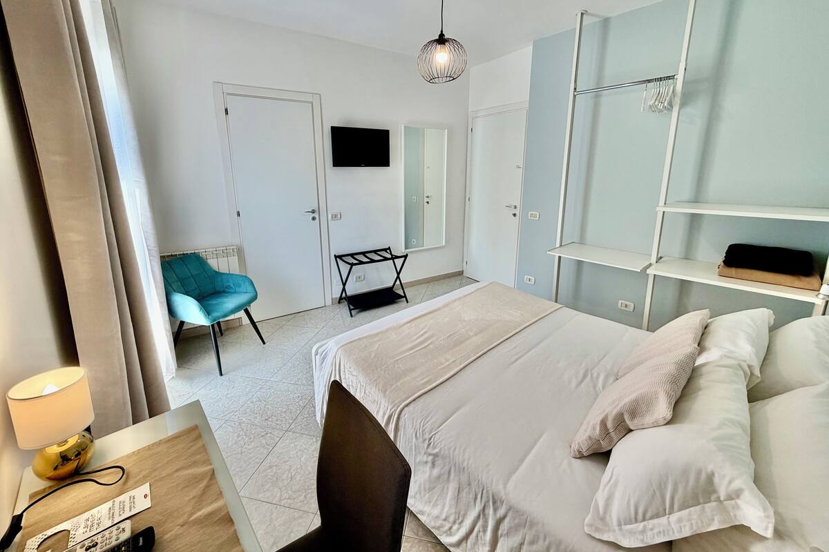 Habitación de hotel con cama, sillón, televisión, armario y escritorio con lámpara.