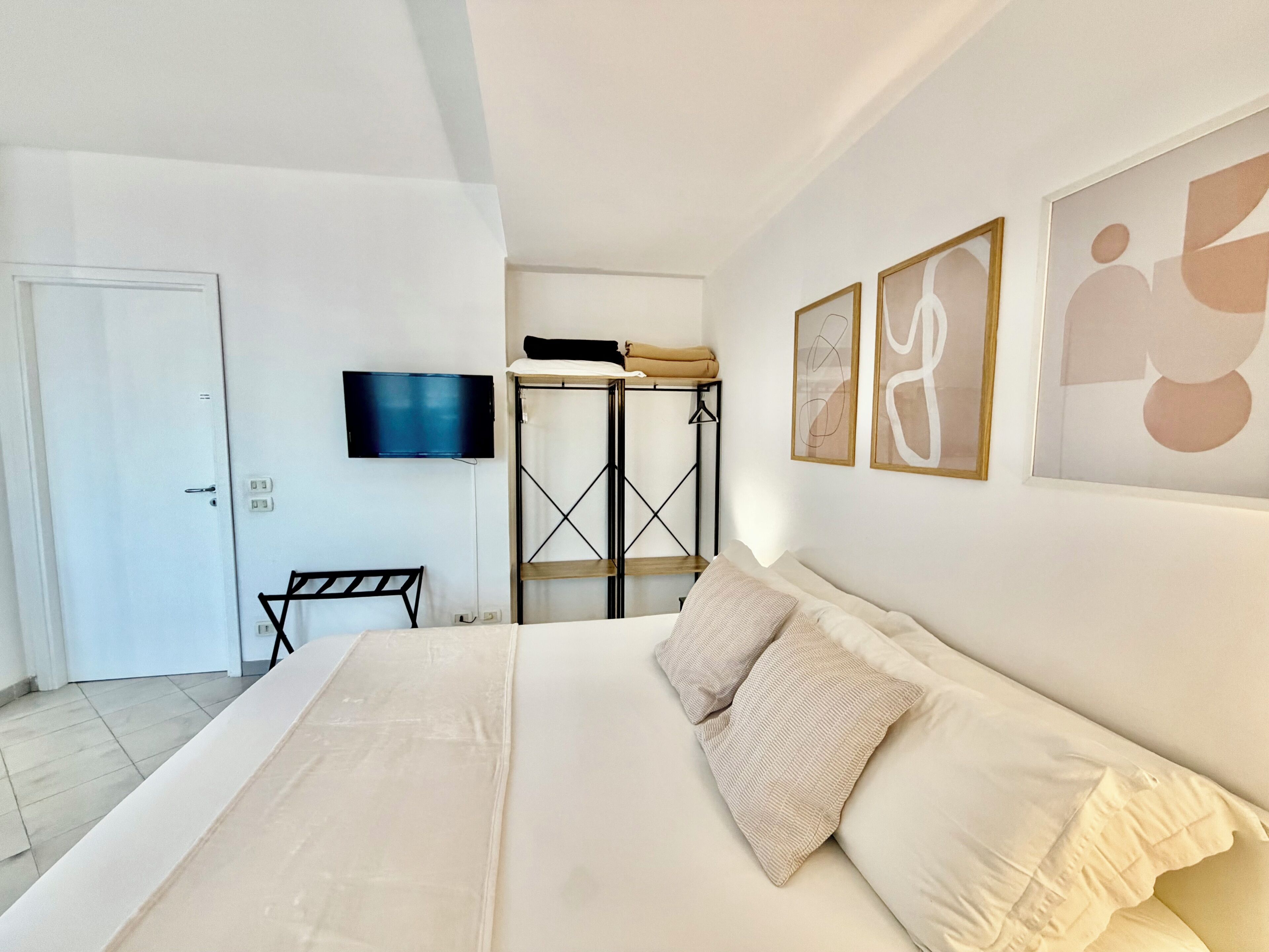 A bedroom with a bed, a TV, a wardrobe, and abstract wall art.