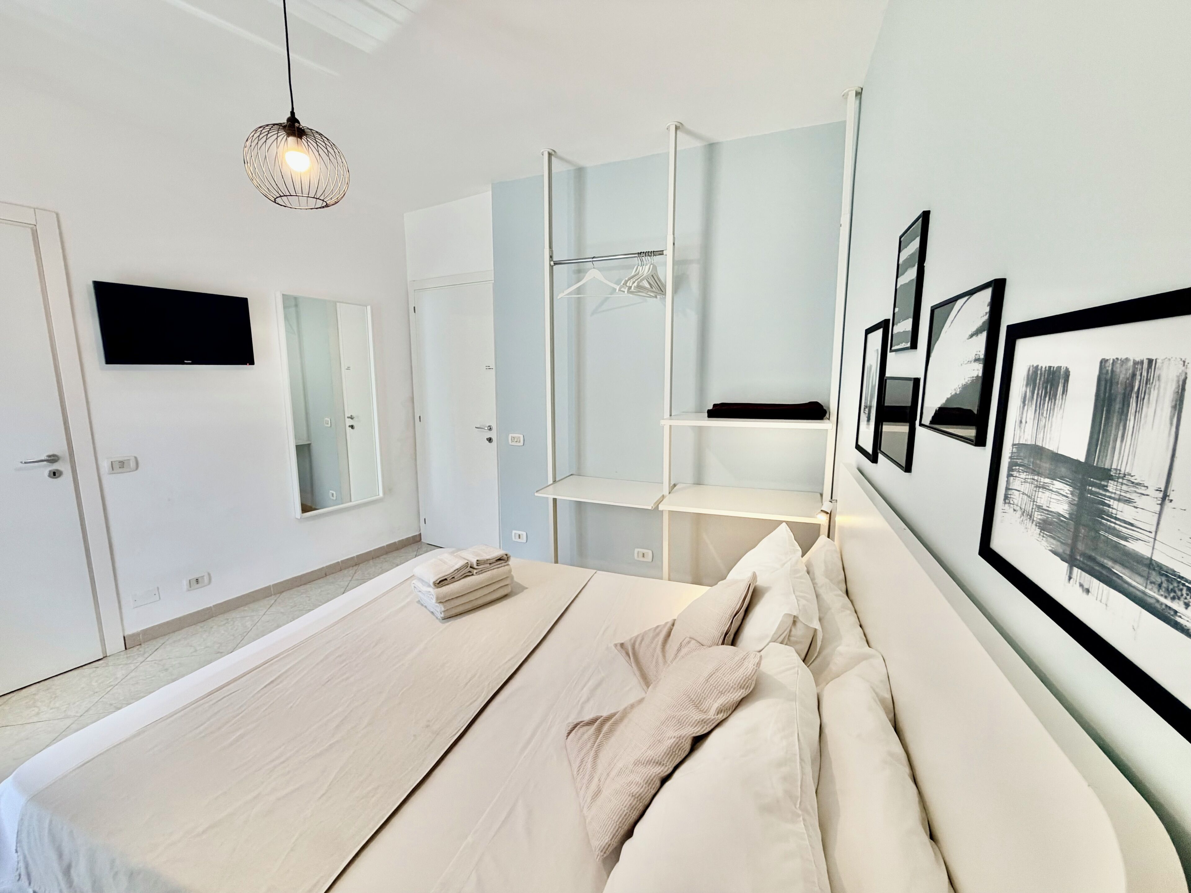 Een moderne slaapkamer met een bed, een hanglamp, een kledingkast en een aan de muur bevestigde televisie.