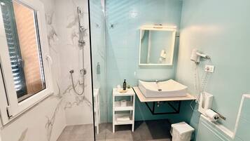 A bathroom with a glass shower enclosure, a white sink, a mirror, and a hairdryer on the wall.