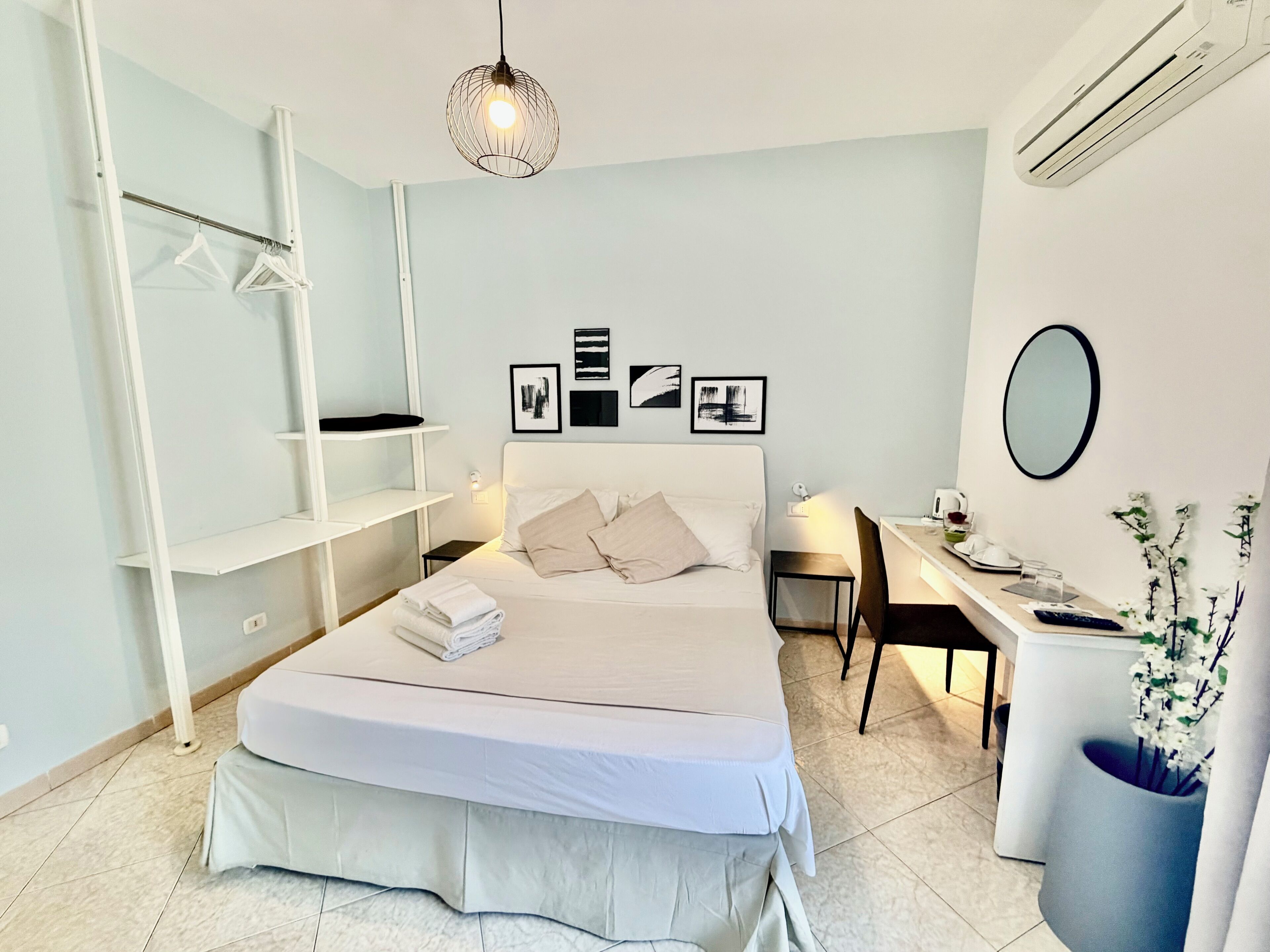 A modern bedroom with a bed, bedside table, desk, chair, and a hanging light fixture.