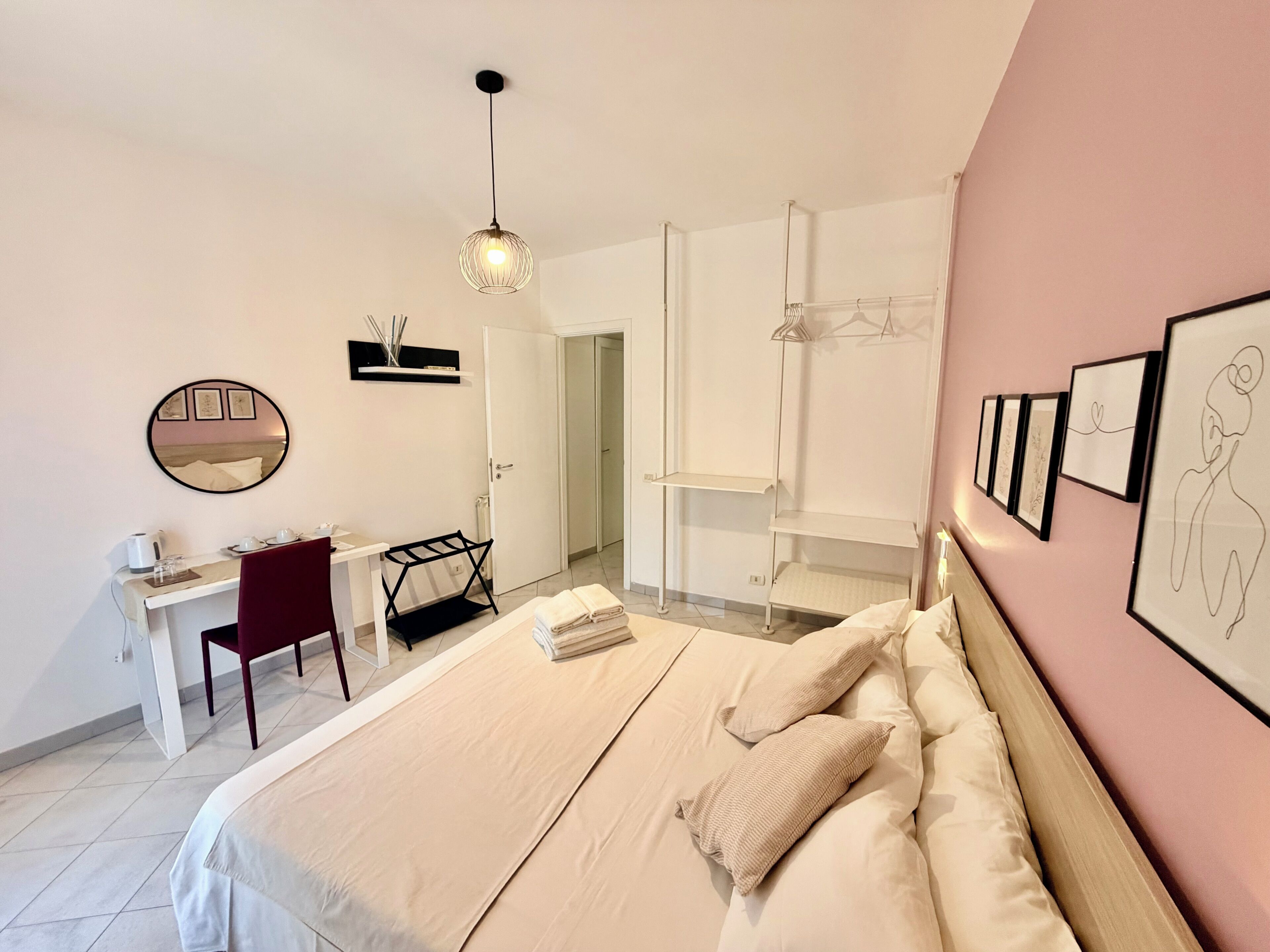 Ein modernes Schlafzimmer mit Bett, Schreibtisch, Stuhl, einer Pendelleuchte und einer Tür zu einem anderen Raum.