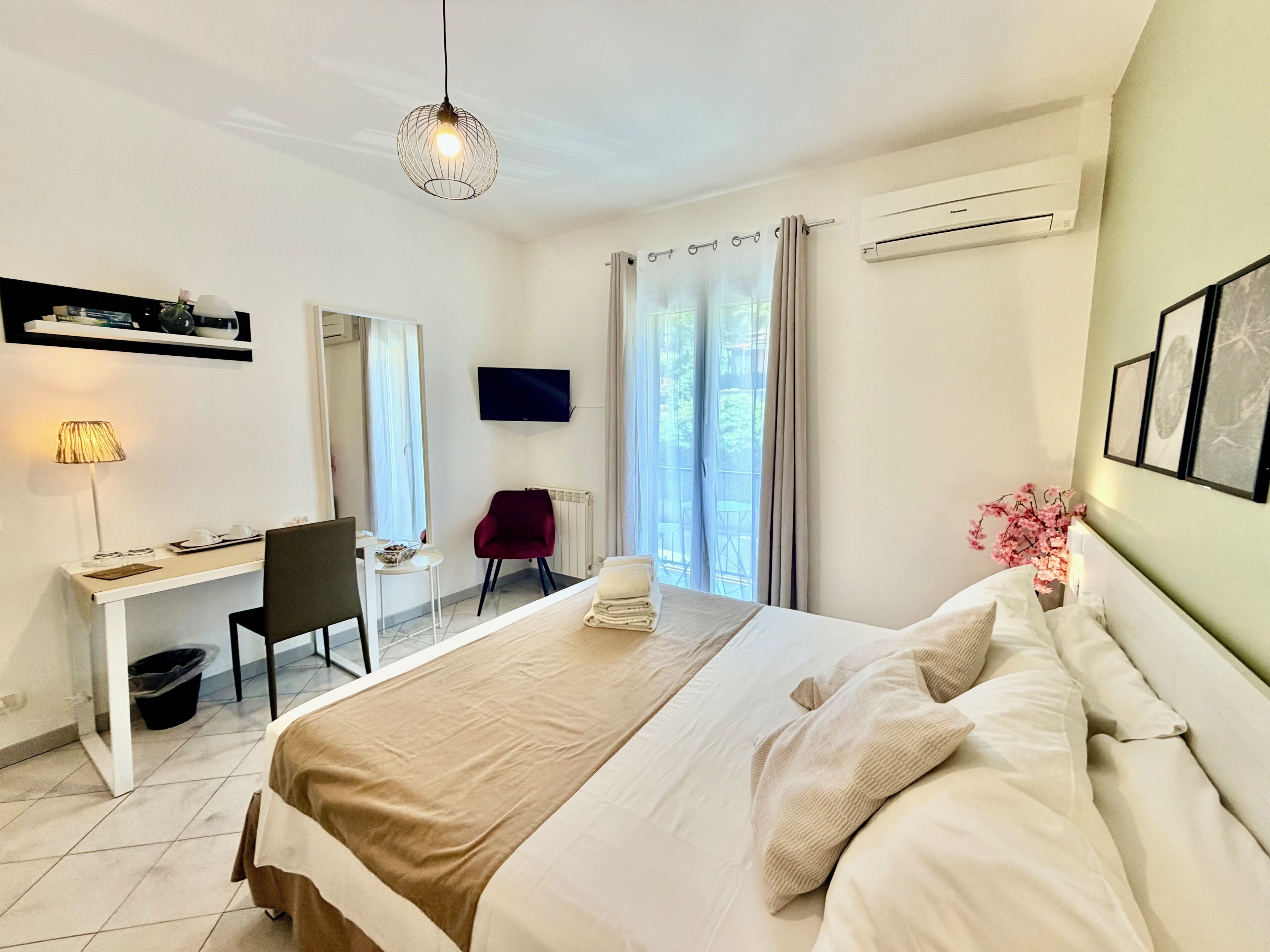 Habitación de hotel con cama, escritorio, silla, televisor, aire acondicionado y ventana con cortinas.