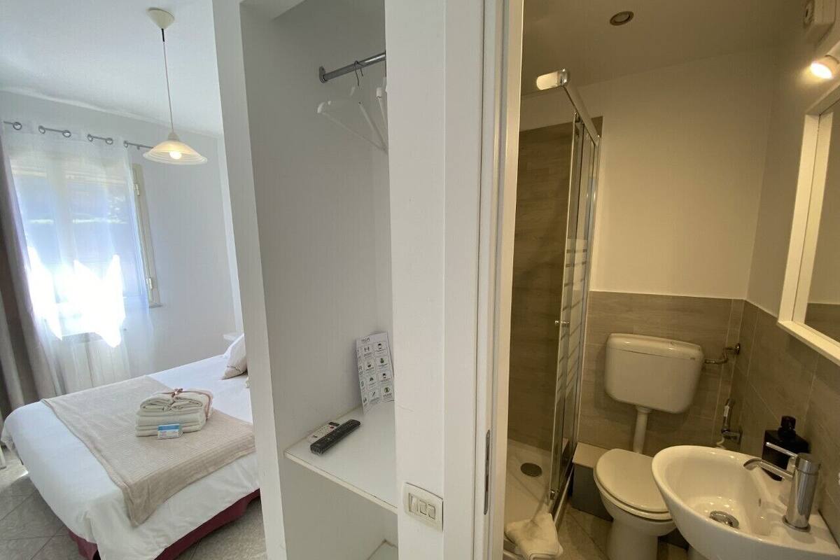 Habitación de hotel con cama, ducha, inodoro y lavabo.