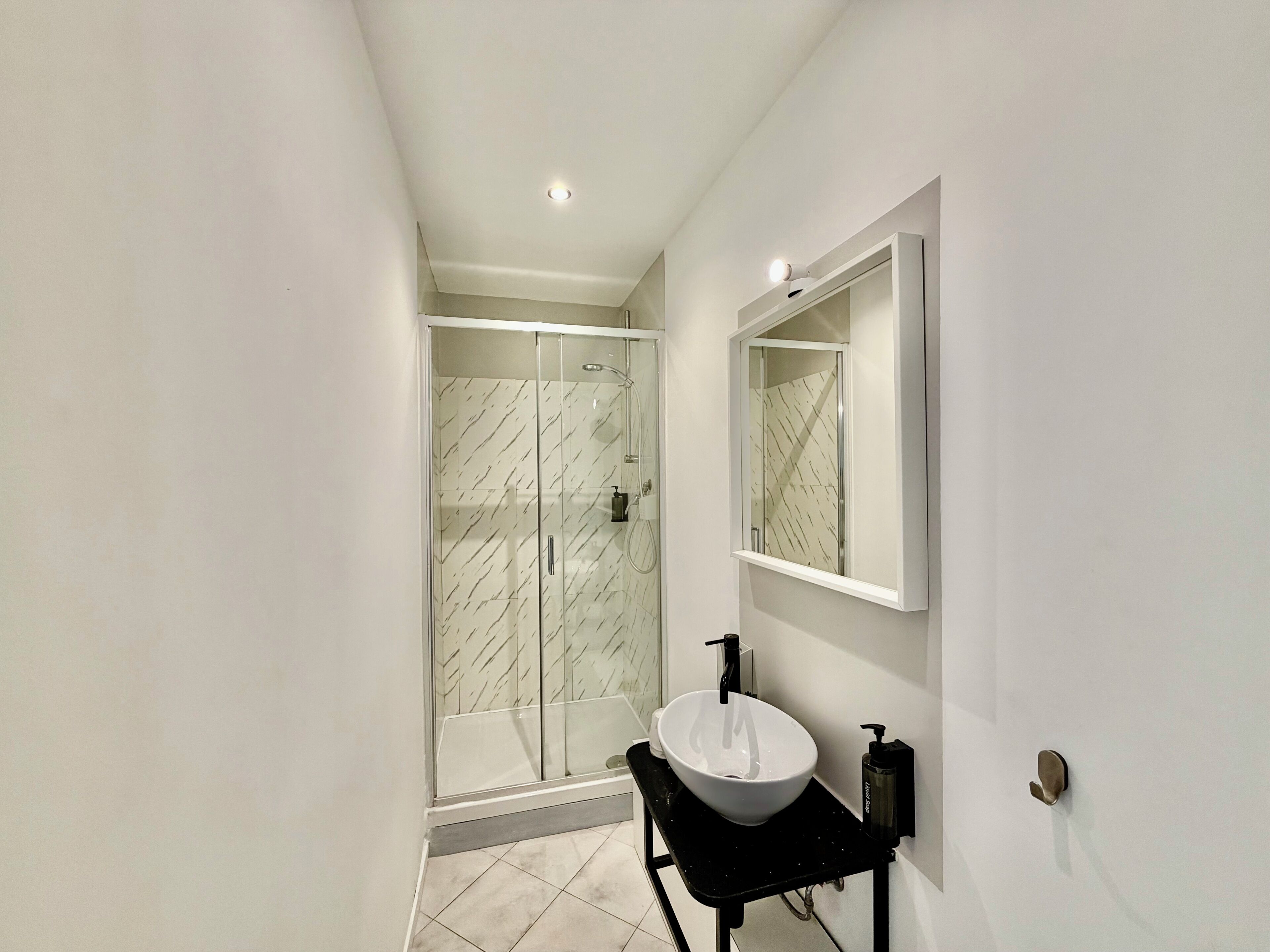 A modern bathroom with a glass-enclosed shower, a white sink, and a mirror.