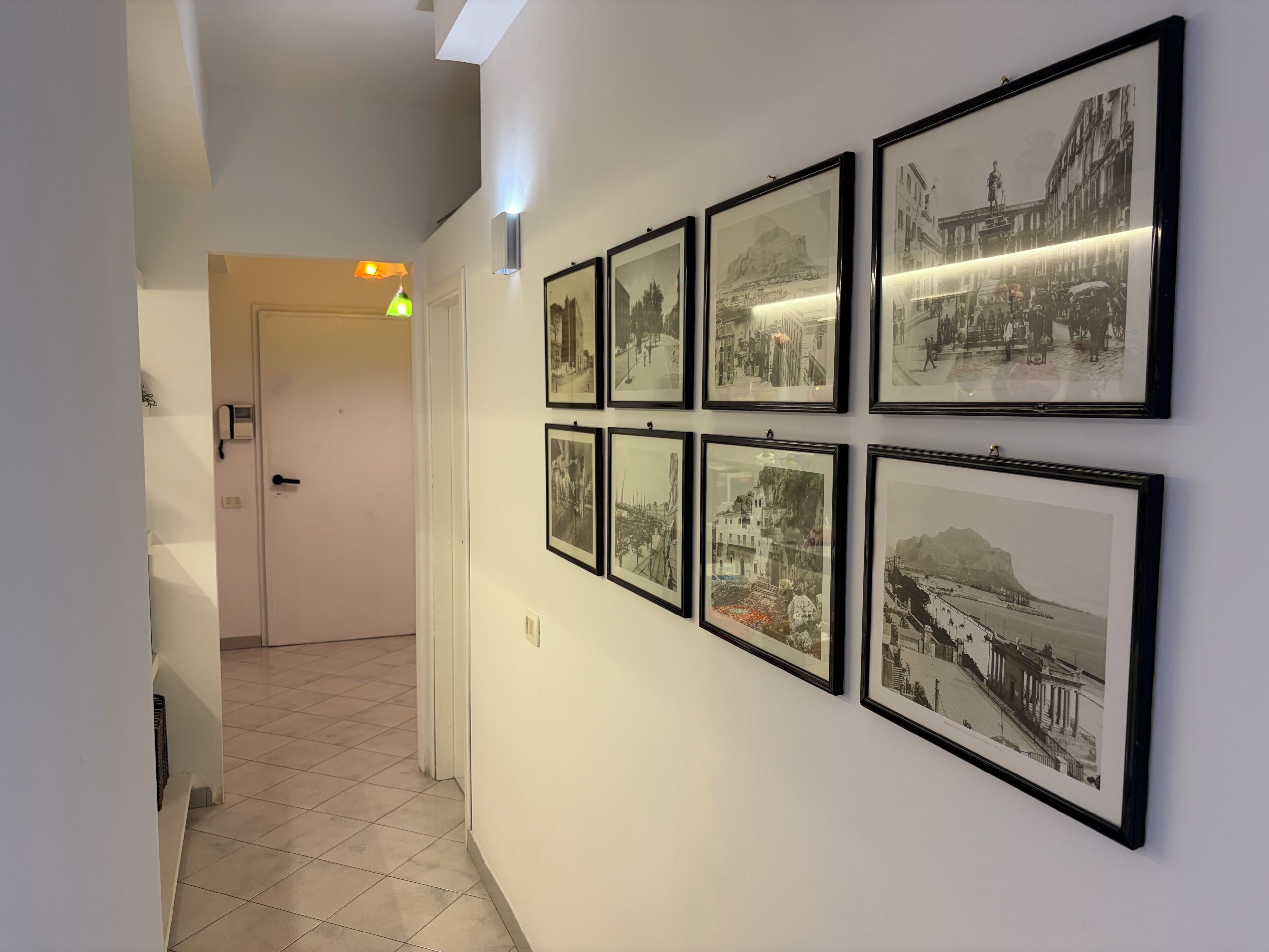 A hallway with framed black and white photographs on the wall, a door at the end, and a light fixture above.