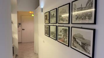 A hallway with framed black and white photographs on the wall, a door at the end, and a light fixture above.