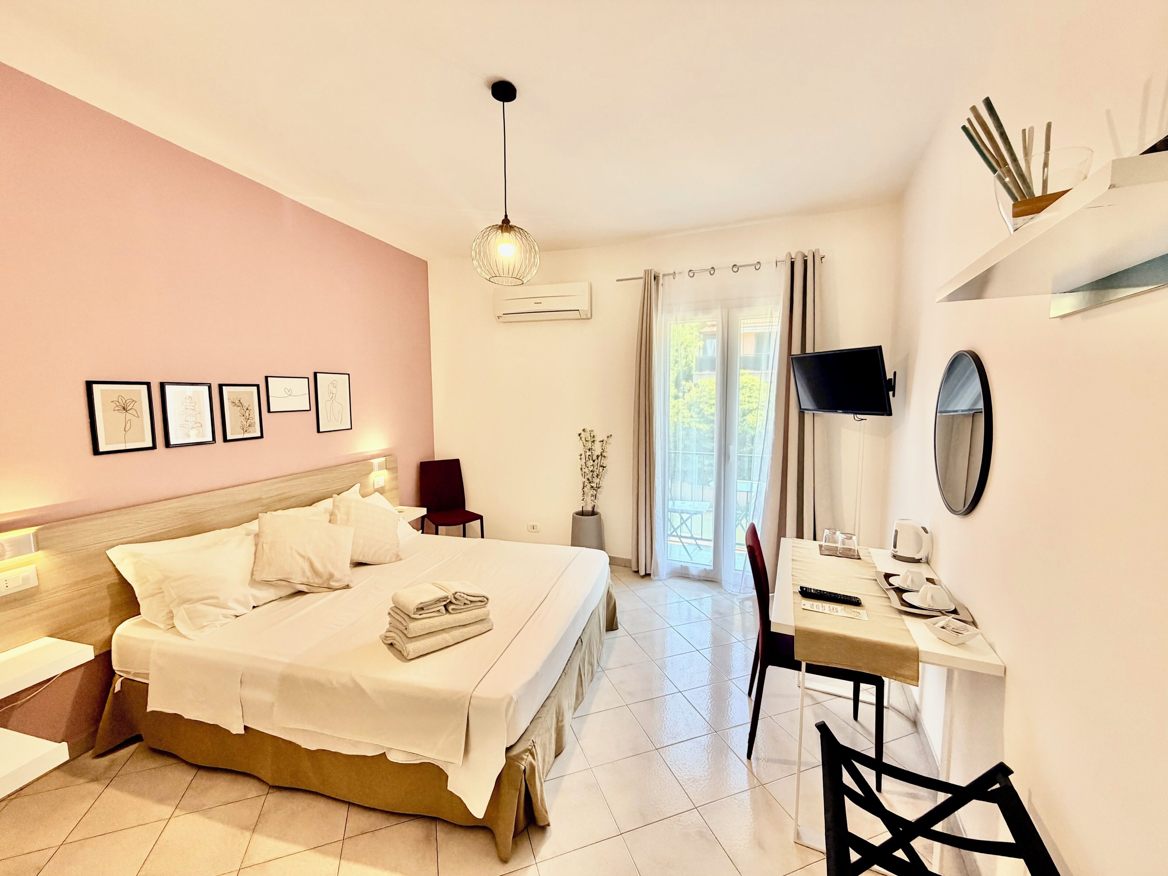 A hotel room with a bed, bedside table, desk, chair, TV, and artwork on the wall.