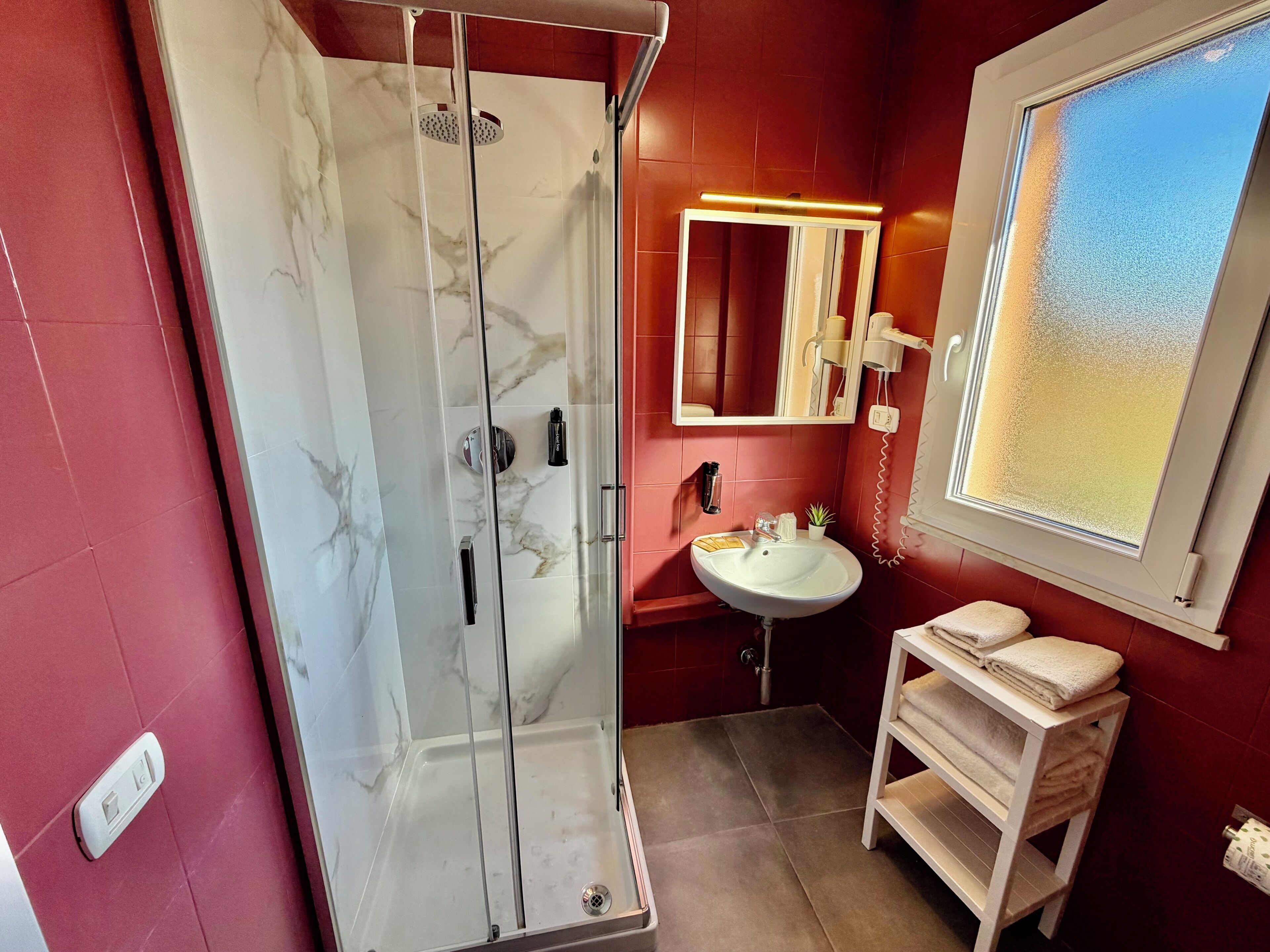 Une salle de bain avec une douche à parois de verre, un lavabo, un miroir et une fenêtre.