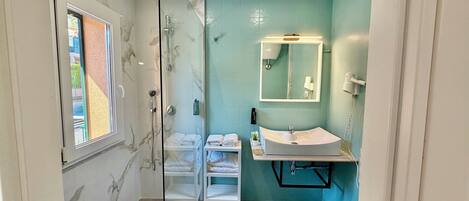 A bathroom with a glass shower enclosure, a white sink with a mirror, and a view of the outside through a window.