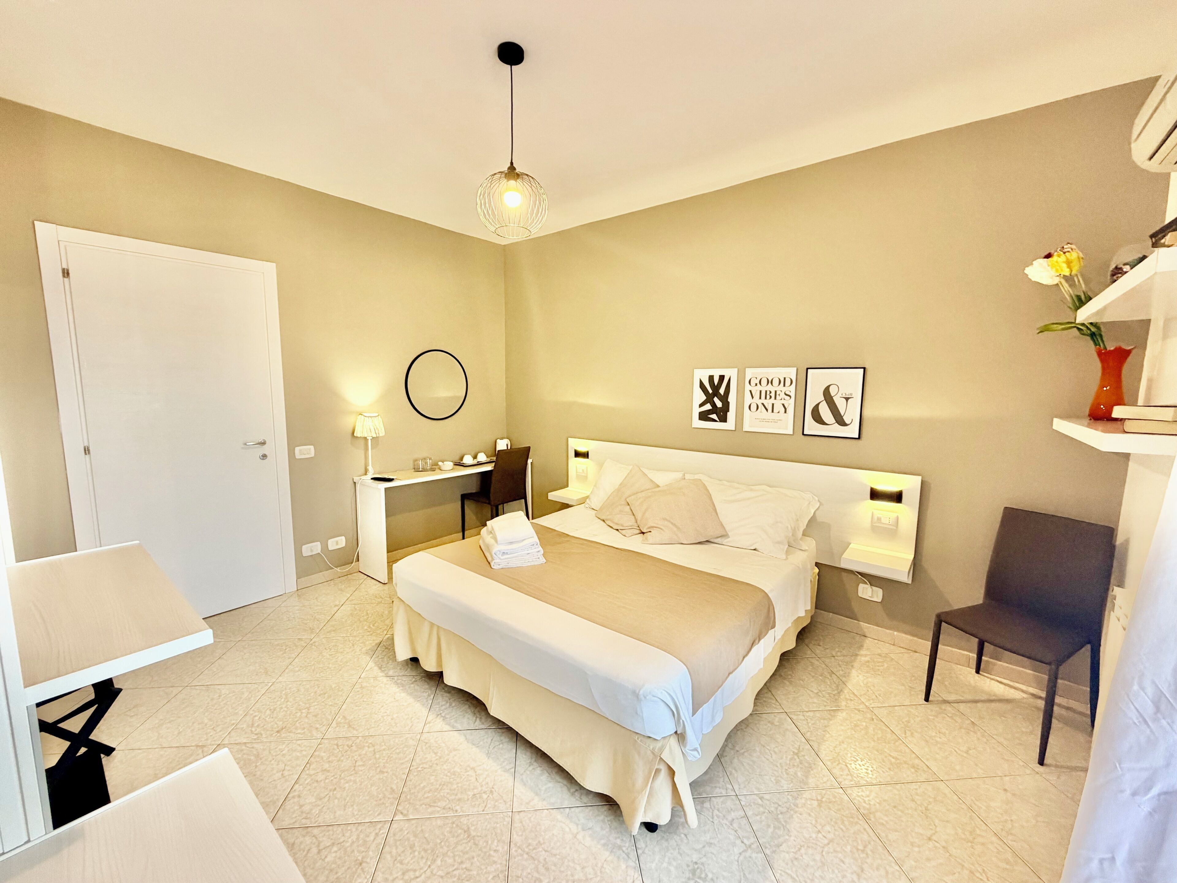 Une chambre d’hôtel comprenant un lit, des tables de chevet, un bureau, une chaise et un luminaire suspendu.