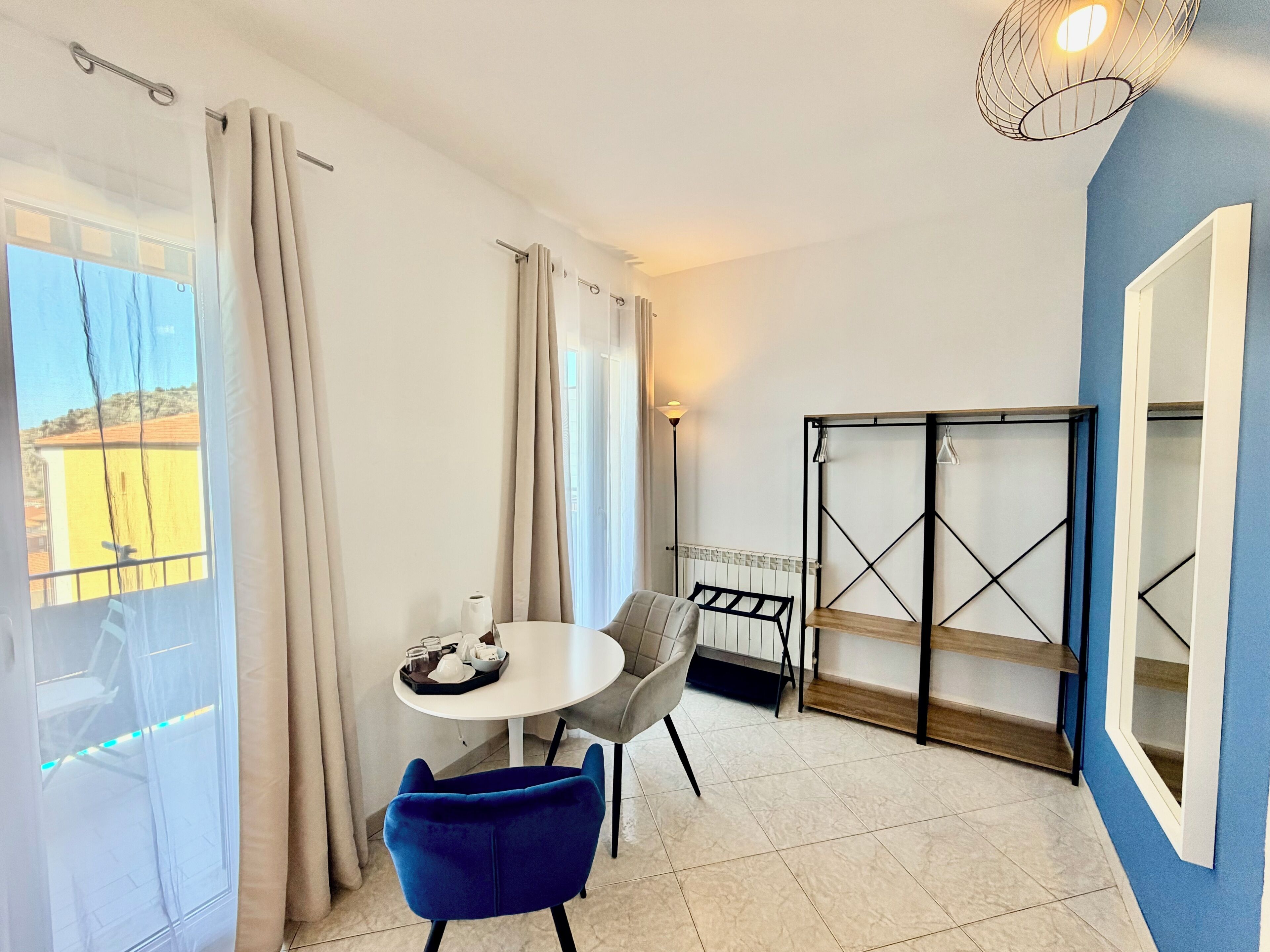 A room with a table, chairs, a radiator, a shelf unit, and a view through a window.