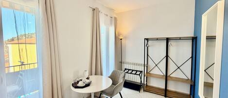 A room with a table, chairs, a radiator, a shelf unit, and a view through a window.