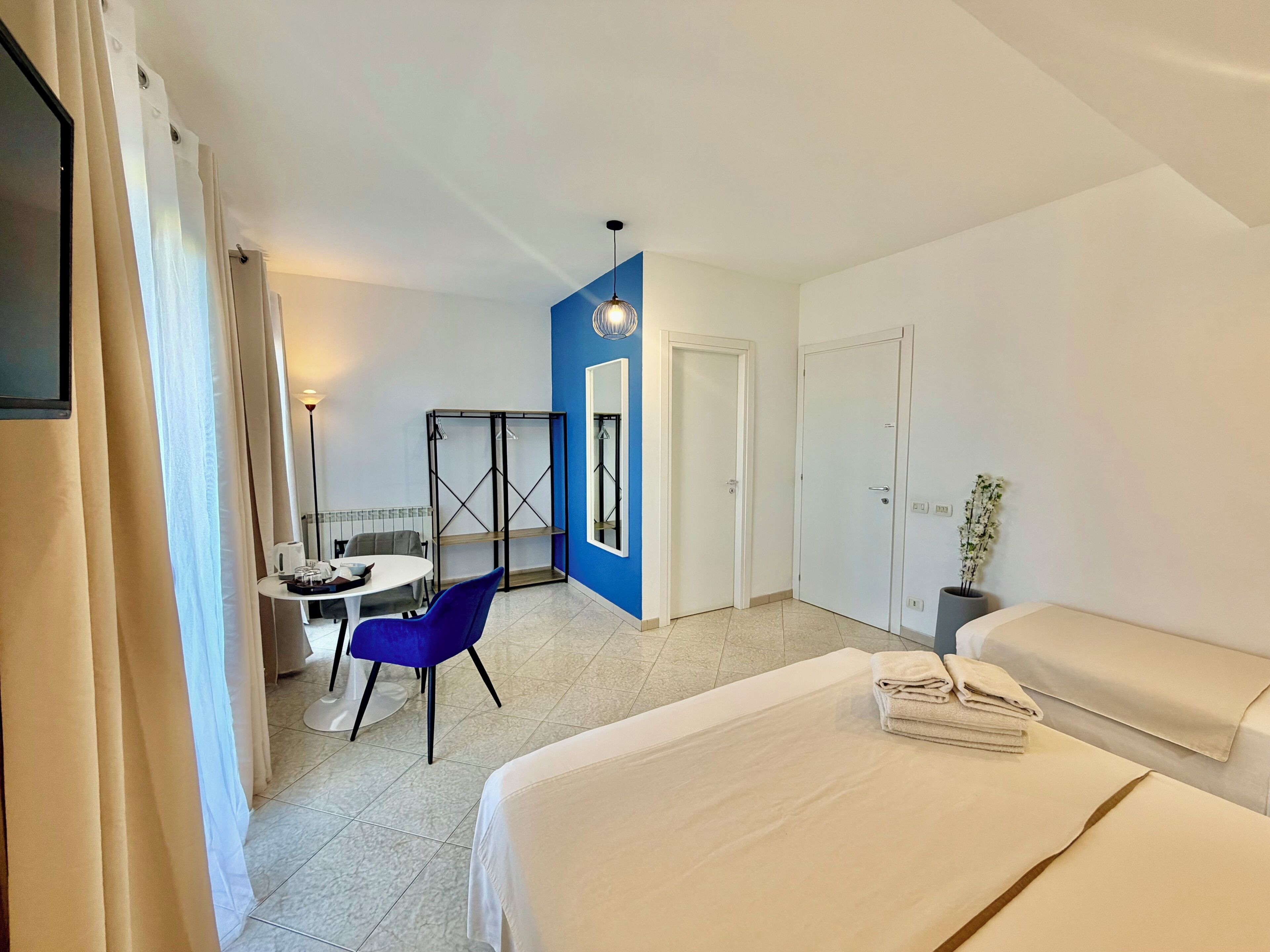 A hotel room with a bed, a desk with a chair, a wardrobe, and a plant.
