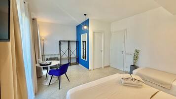 A hotel room with a bed, a desk with a chair, a wardrobe, and a plant.