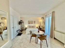 Habitación de hotel con cama, escritorio, televisor y zona de comedor con sillas.