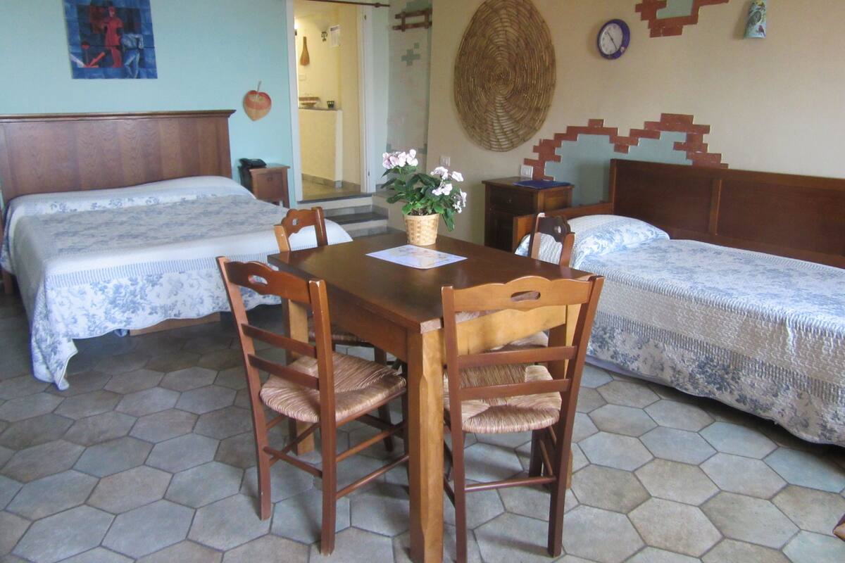 Une pièce avec deux lits, une table à manger en bois et des chaises. On y trouve également une horloge murale et un élément décoratif suspendu au mur.