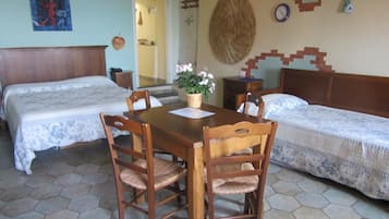 Ein Zimmer mit zwei Betten, einem Holzesstisch und Stühlen. An der Wand hängt eine Uhr und ein dekoratives Wandbild.