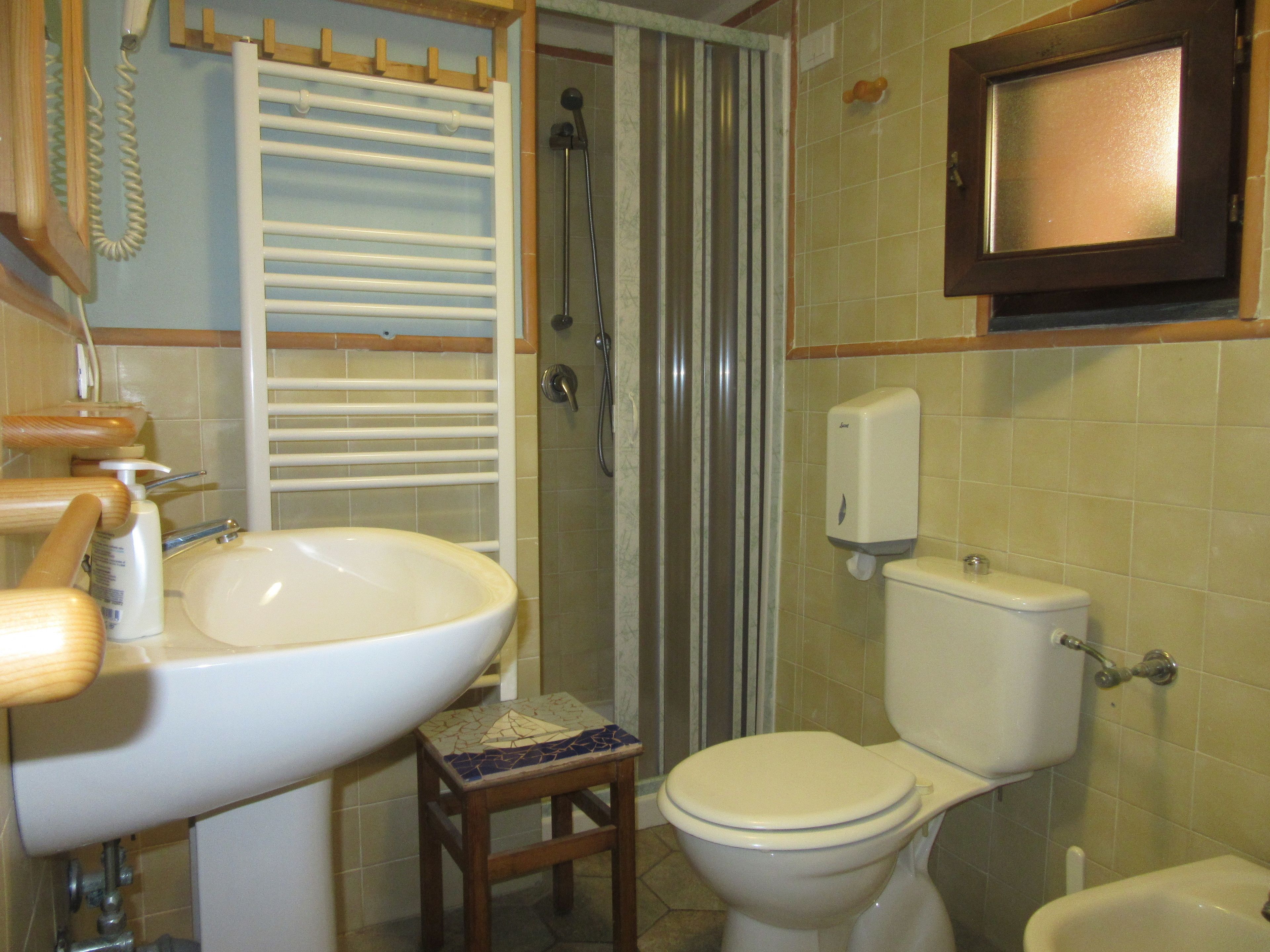 A bathroom with a sink, toilet, shower, and a soap dispenser.