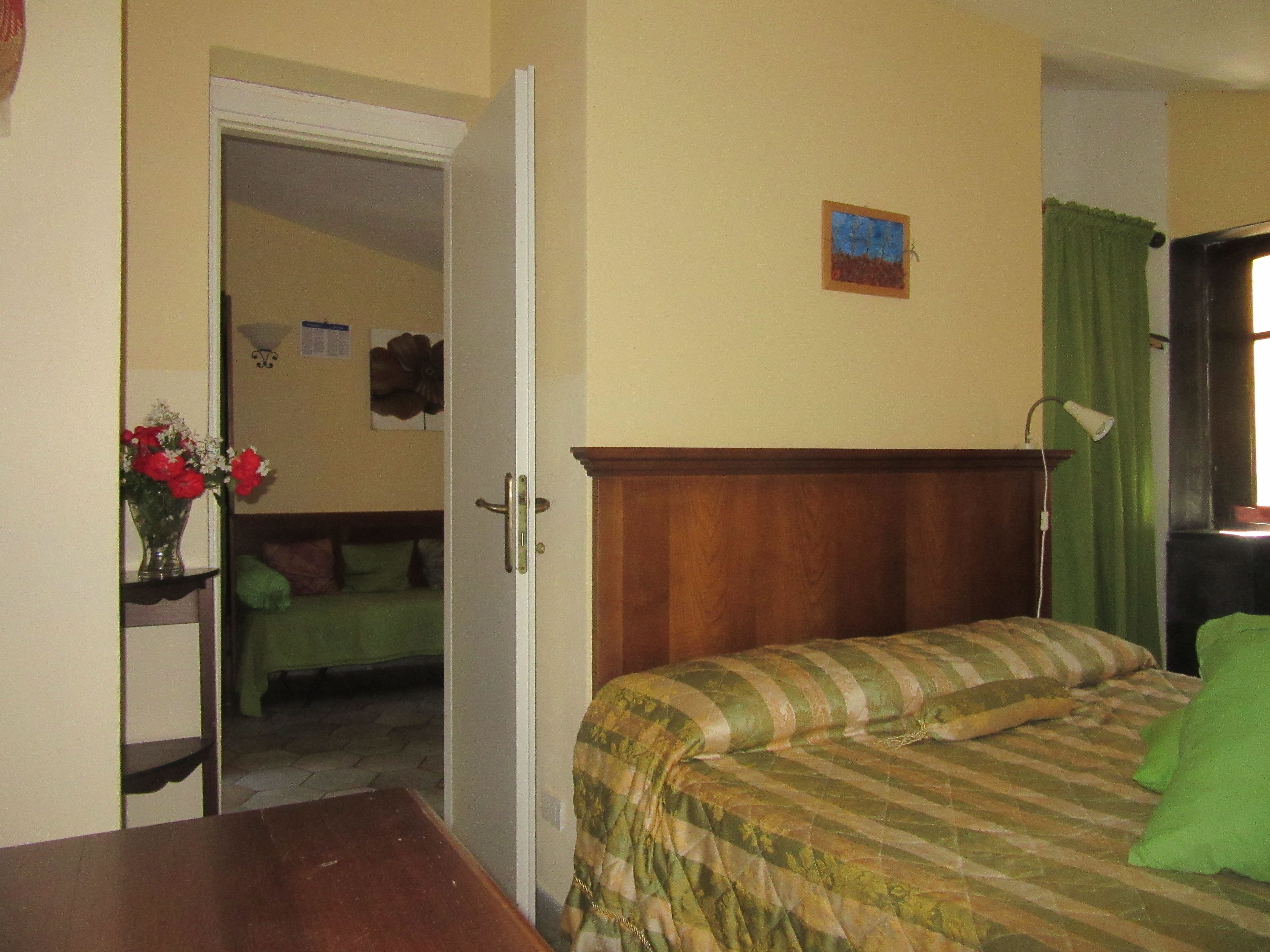 A bedroom with a bed, a wooden headboard, a green curtain, a nightstand, and a vase with flowers.
