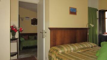 A bedroom with a bed, a wooden headboard, a green curtain, a nightstand, and a vase with flowers.