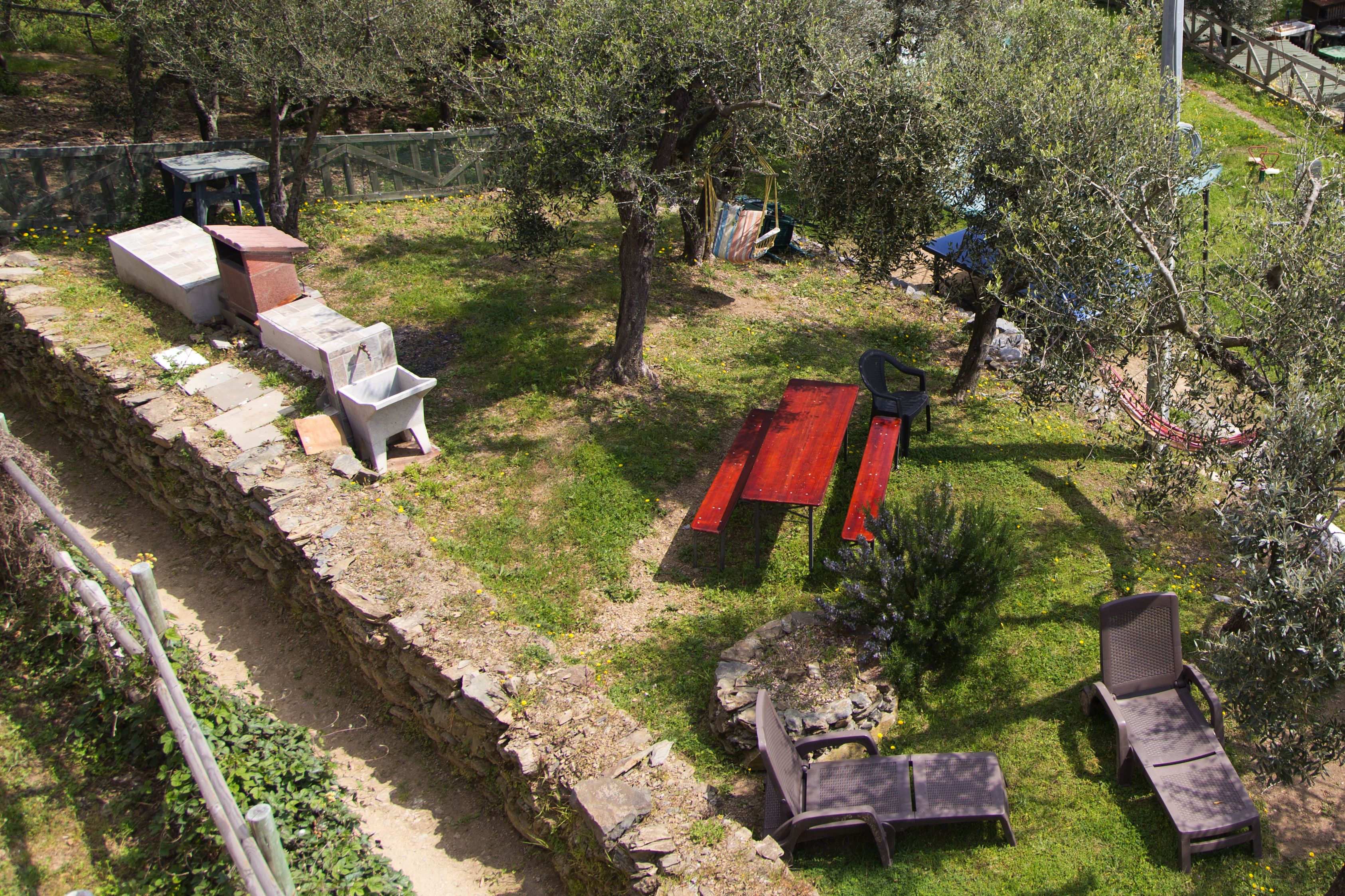 A garden with a stone bench, a red picnic table, and a small tree.