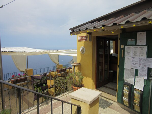A reception area with a view of the sea, a balcony with outdoor seating, and a sign indicating a reception. - Il Borgo di Campi (Riomaggiore)