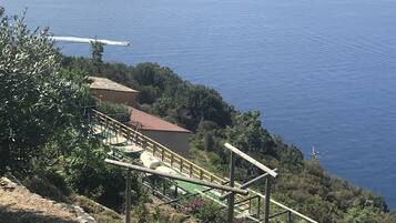 A coastal area with a staircase leading down to a beach, surrounded by greenery and a clear view of the sea.