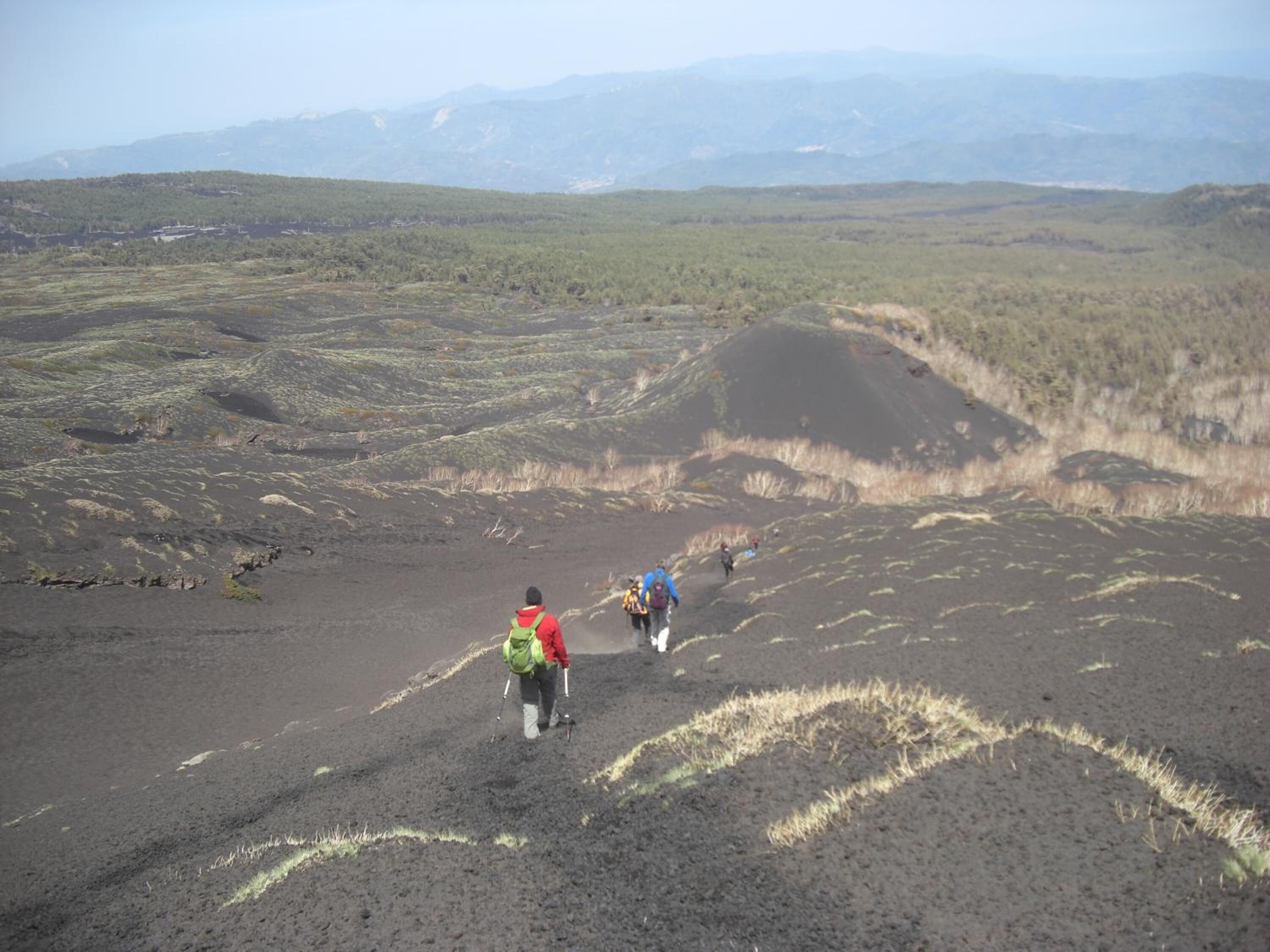 A group of hikers on a volcanic terrain with distant mountains.