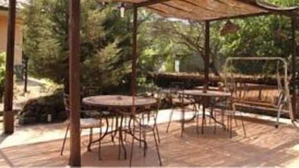 An outdoor patio with a wooden table and chairs, surrounded by greenery. - Sotto il Vulcano (Nicolosi)