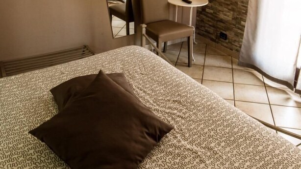 A hotel room with a bed, a television mounted on the wall, a small table, and a chair. - Sotto il Vulcano (Nicolosi)
