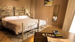 A hotel room with a bed, a nightstand, a table with books, and a wall with a mirror and artwork. - Sotto il Vulcano (Nicolosi)