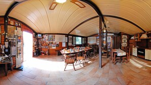 A spacious room with a curved ceiling, wooden walls, and a central dining area with multiple chairs and tables. - Sotto il Vulcano (Nicolosi)