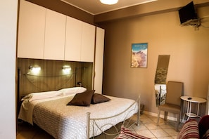 A bedroom with a bed, a chair, a small table, and a TV mounted on the wall. - Sotto il Vulcano (Nicolosi)