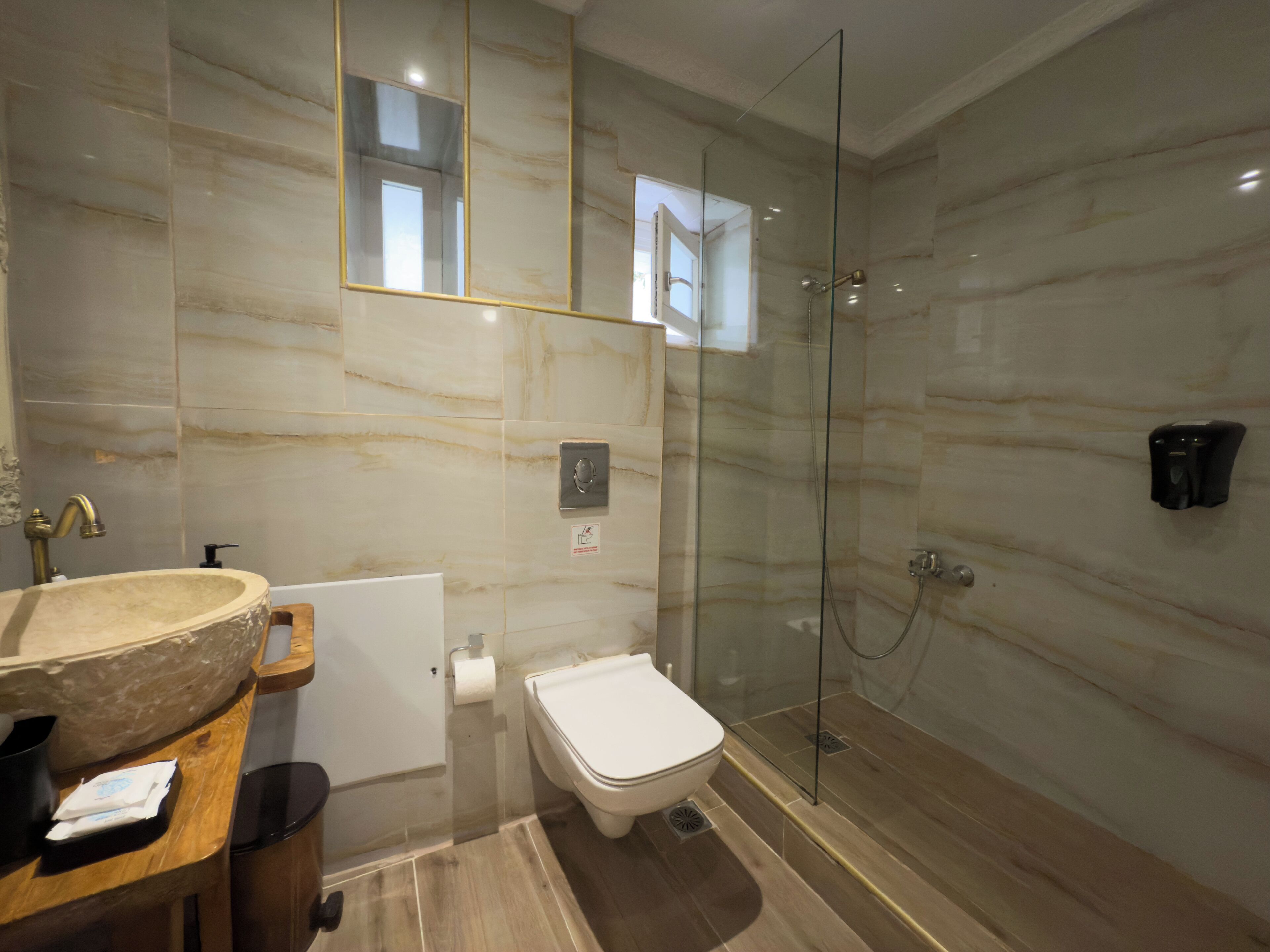 A modern bathroom with a marble wall, a glass-enclosed shower, a sink with a marble basin, and a toilet.
