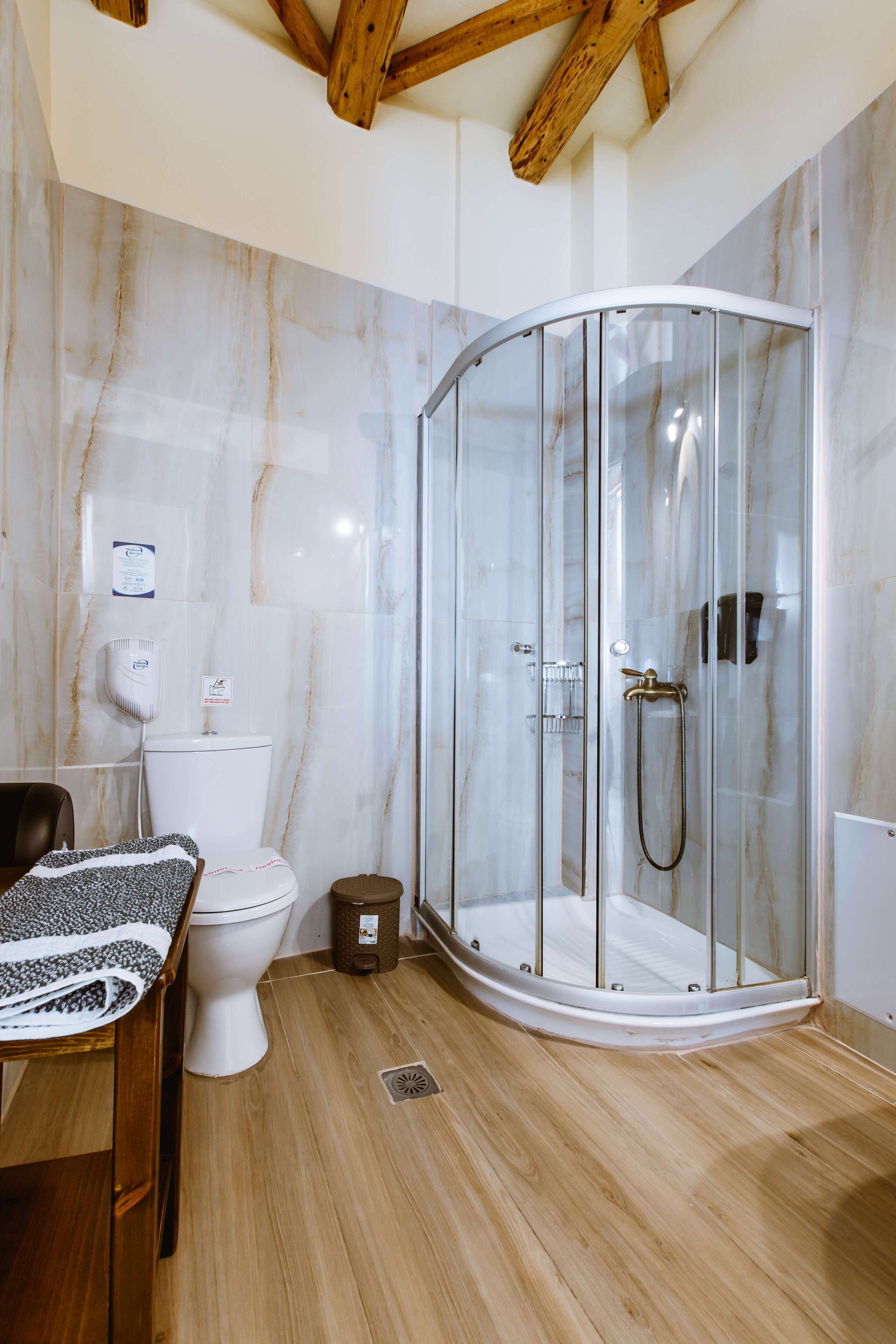 A modern bathroom with a glass-enclosed shower, a toilet, and a wooden floor.