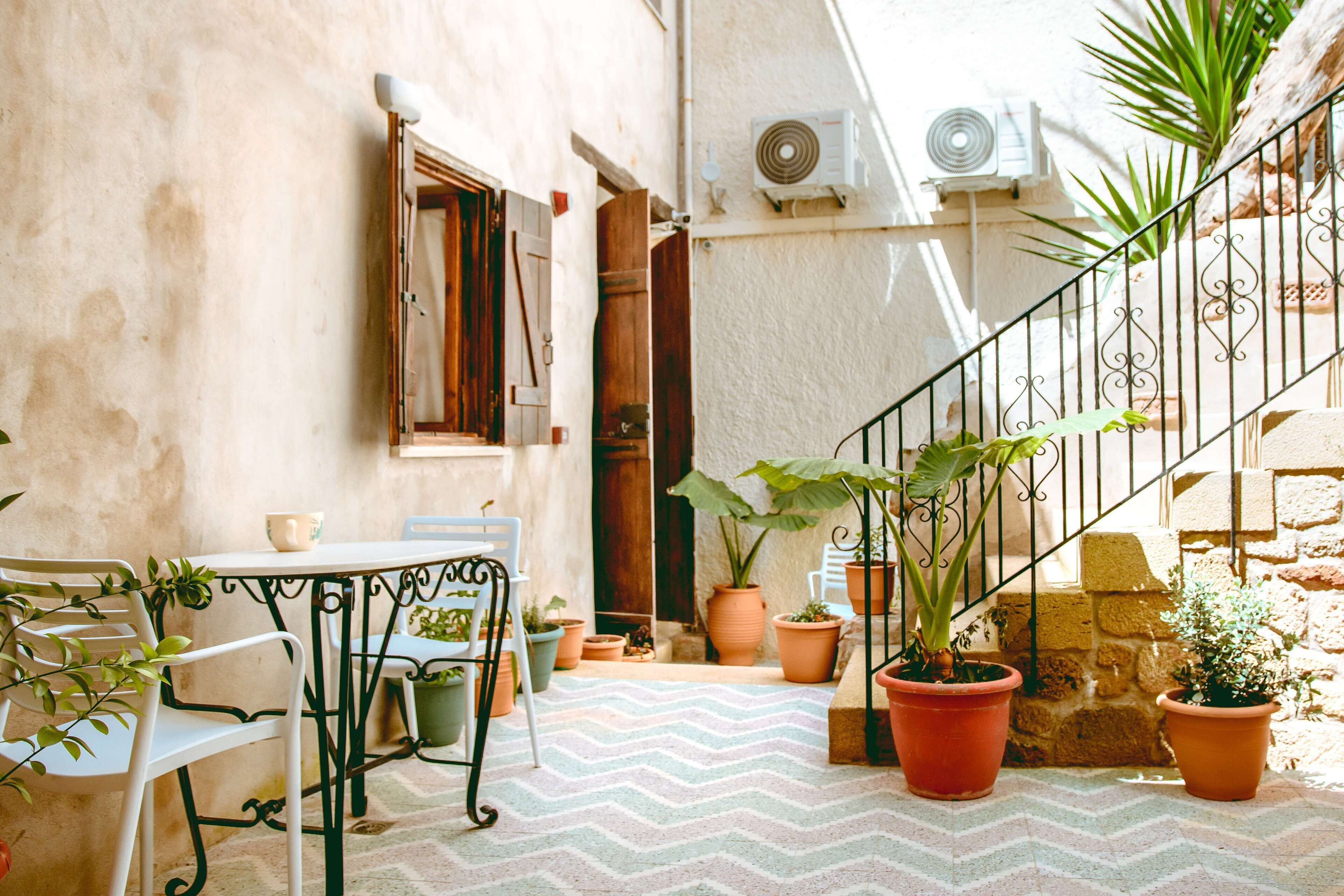 A small outdoor patio with a table and chairs, surrounded by potted plants and a staircase.