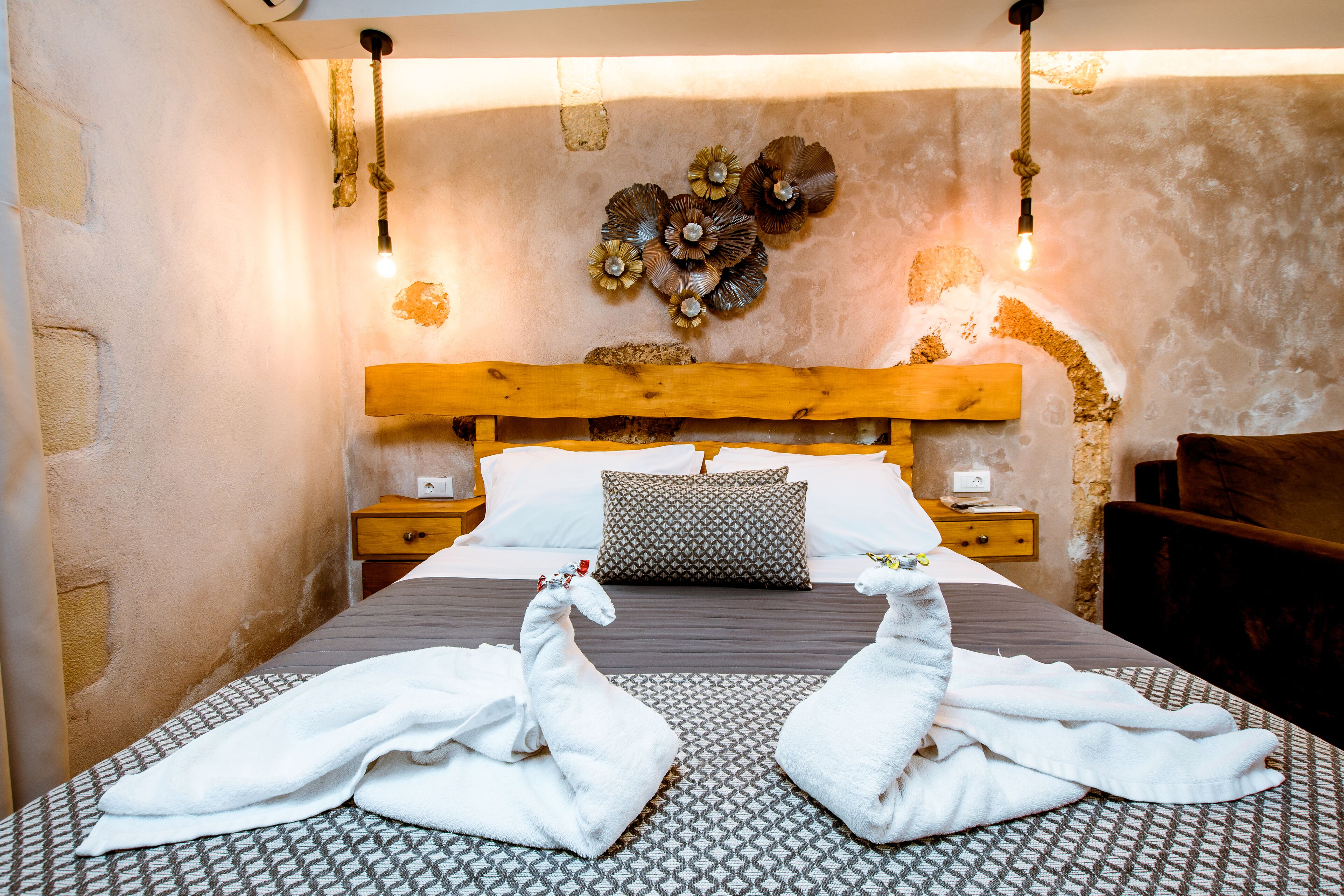 A bed with a wooden headboard, two nightstands, a patterned rug, and towels arranged in swan shapes.