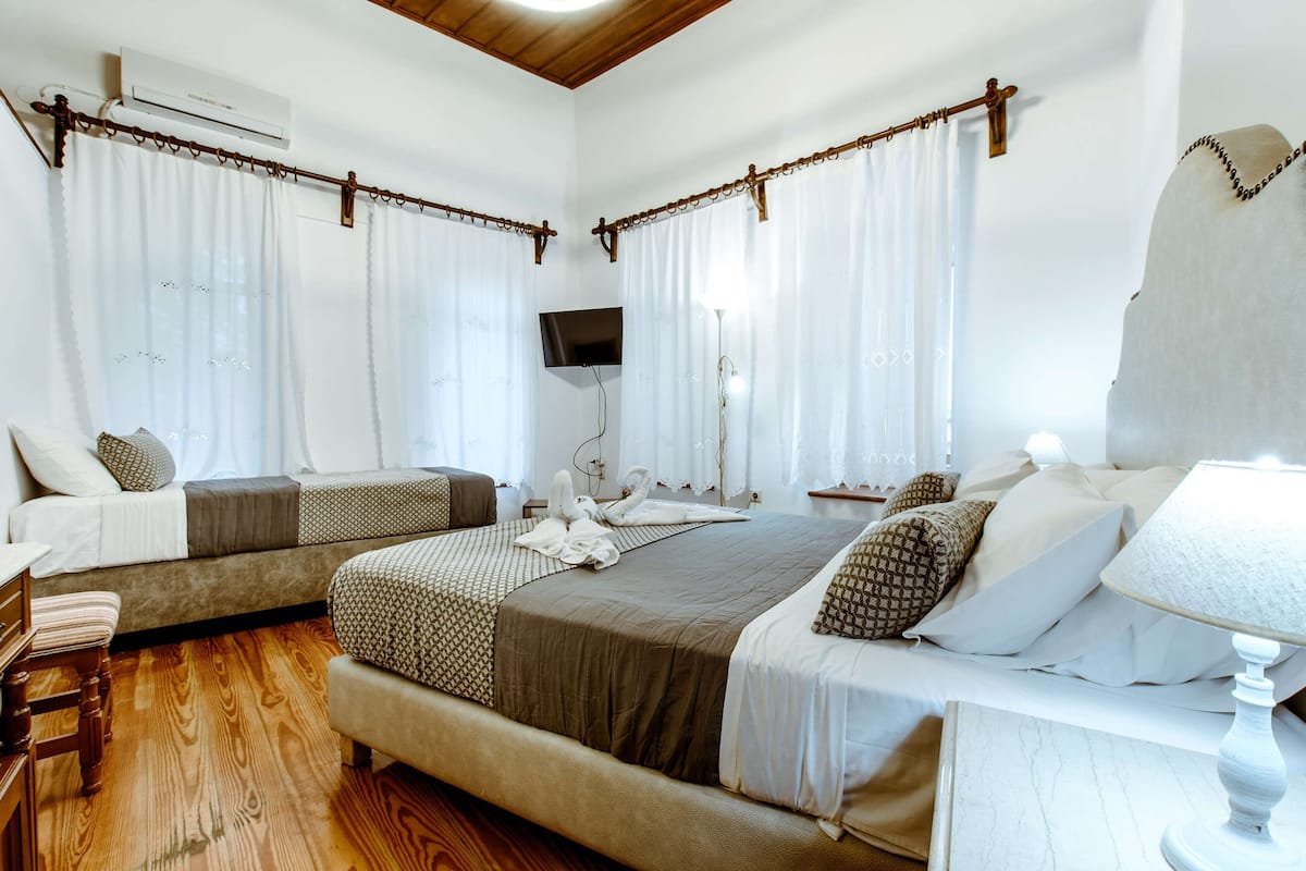 A hotel room with two beds, wooden flooring, a flat-screen TV, and a ceiling fan.