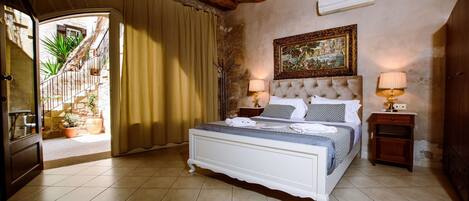A bedroom with a bed, two bedside tables, a painting on the wall, and a door leading to a balcony.