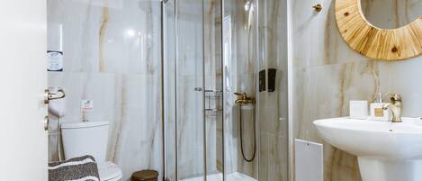 Un baño moderno con ducha de vidrio, un lavamanos blanco y una pared de mármol.