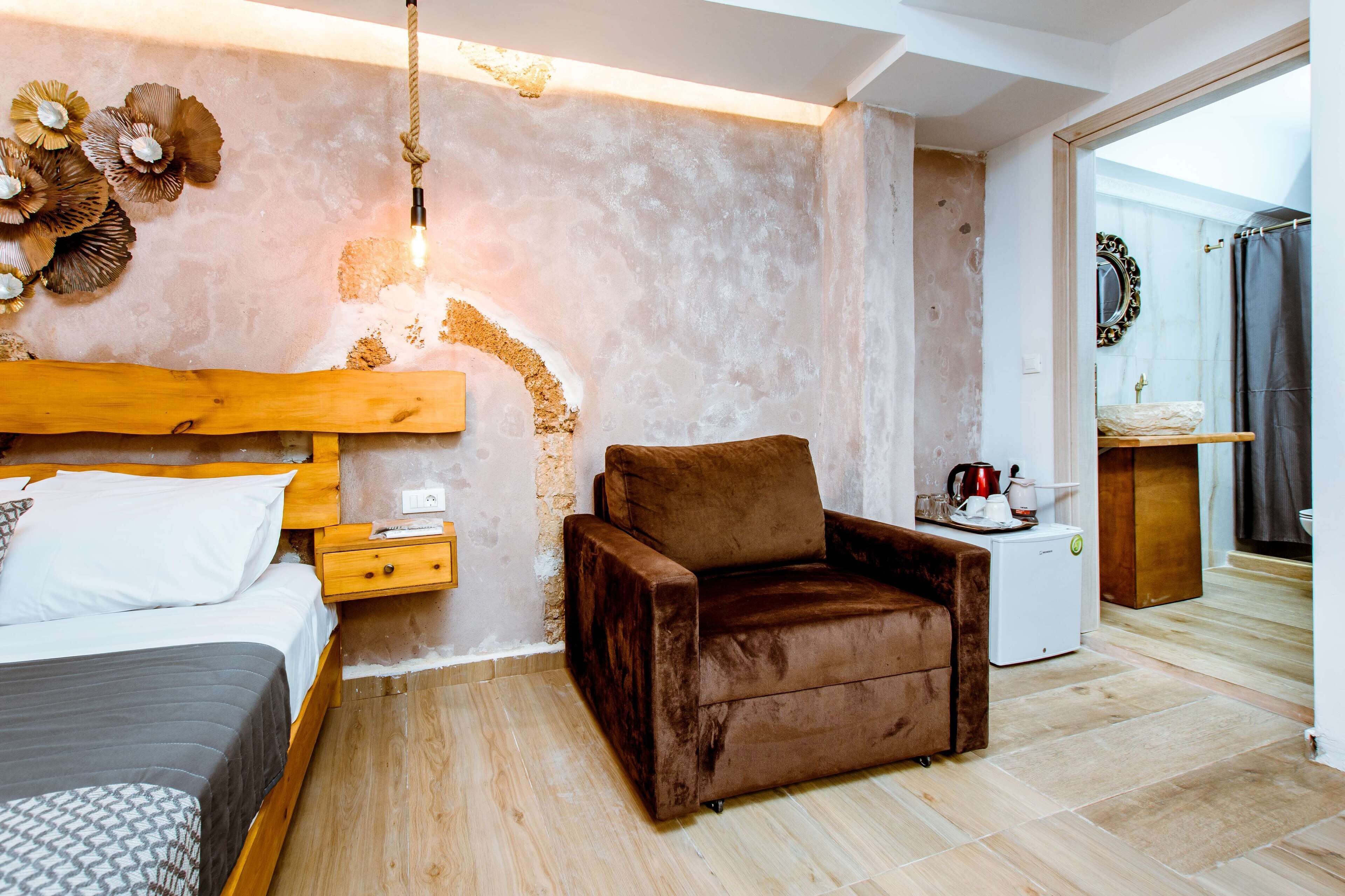 A bedroom with a bed, a brown armchair, a small white table, and a wall-mounted mirror.