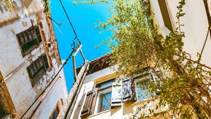 Uma rua estreita com edifícios em ambos os lados, céu azul límpido e alguma vegetação.