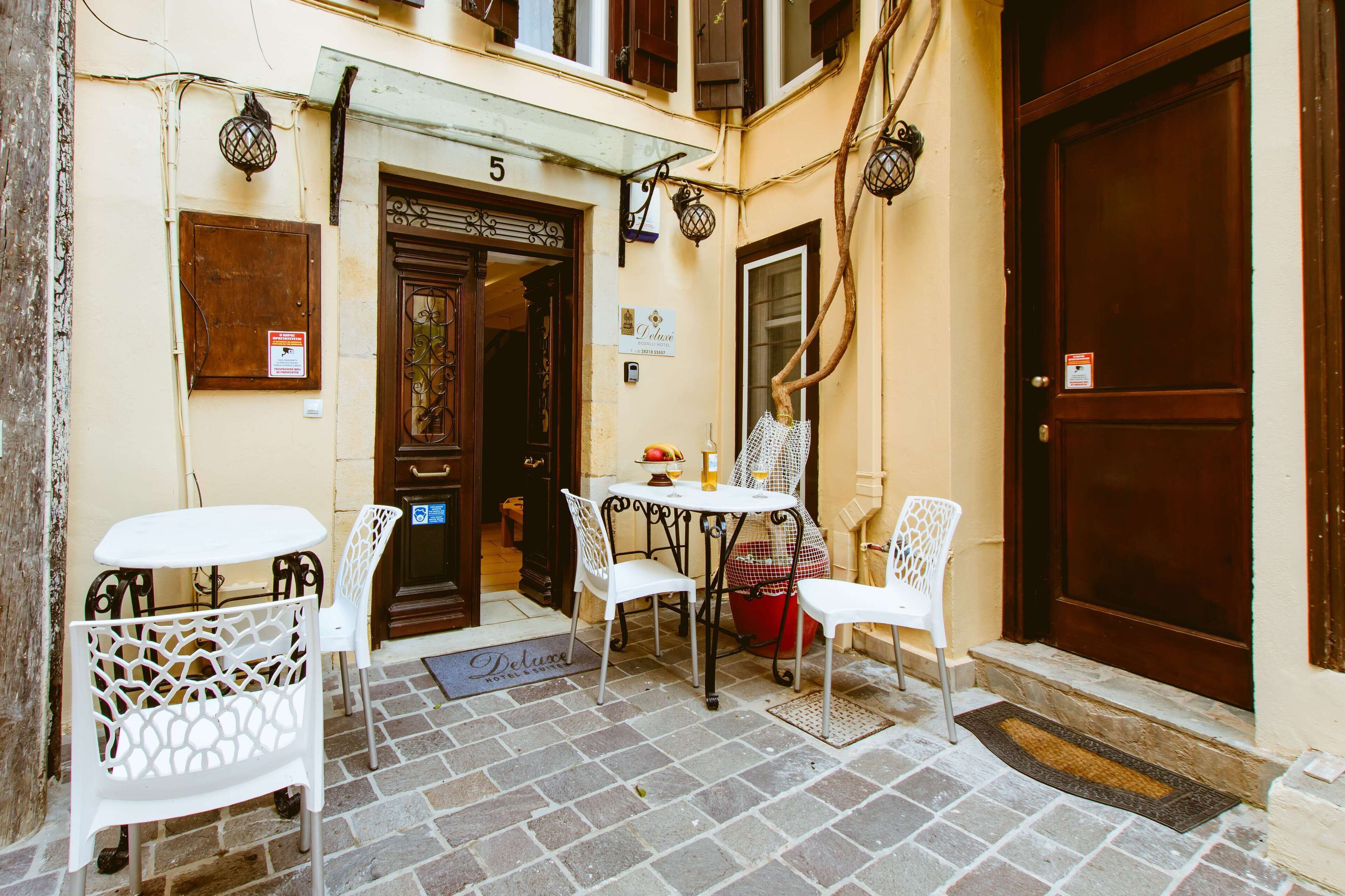 An outdoor seating area with white chairs and a table, a wooden door with the number 5, and a sign indicating a hotel.