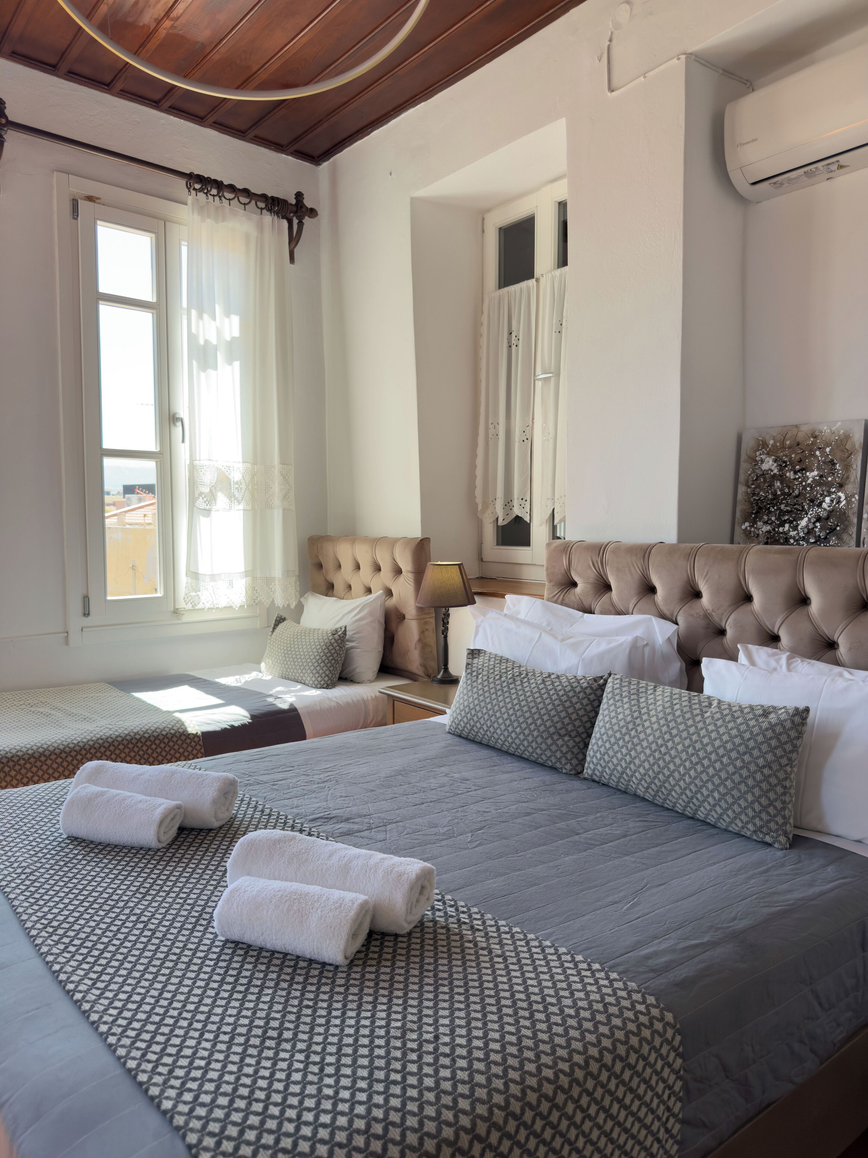 Une chambre d’hôtel avec un grand lit, deux petits lits, un lustre et une fenêtre avec des rideaux.