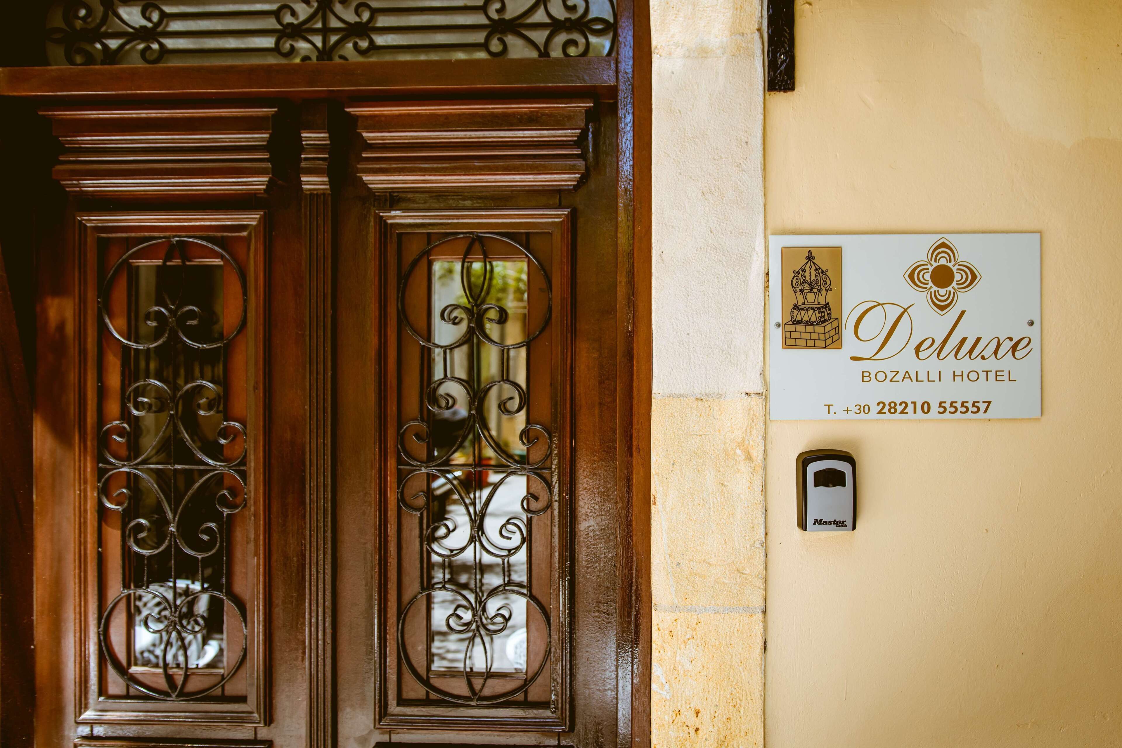 Una puerta de madera con ornamentación metálica detallada y un letrero del Hotel Deluxe Bozall.