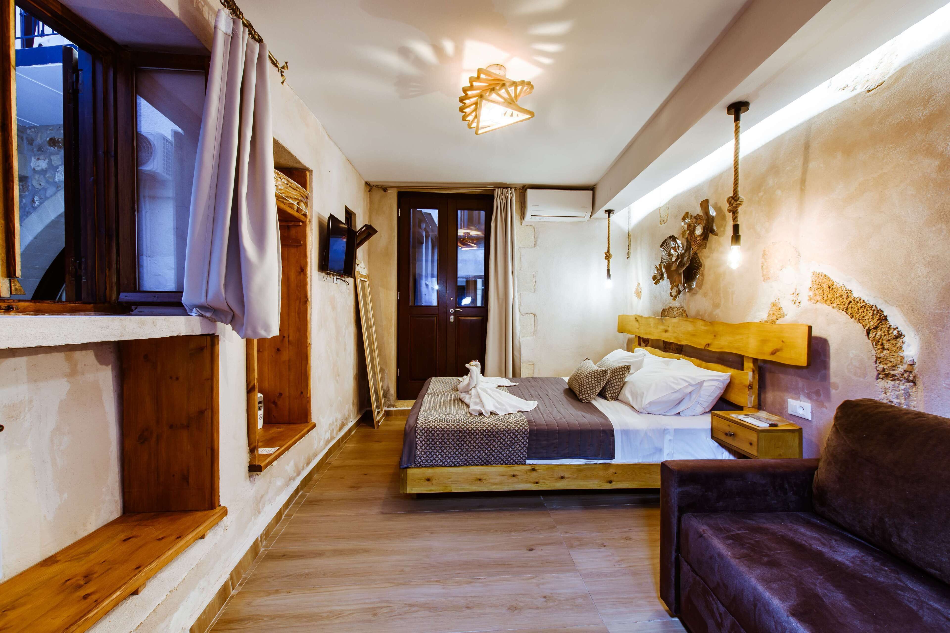 Un dormitorio con cama de madera, una mesita de noche de madera, un sofá marrón, una ventana con cortinas y una lámpara de pared.