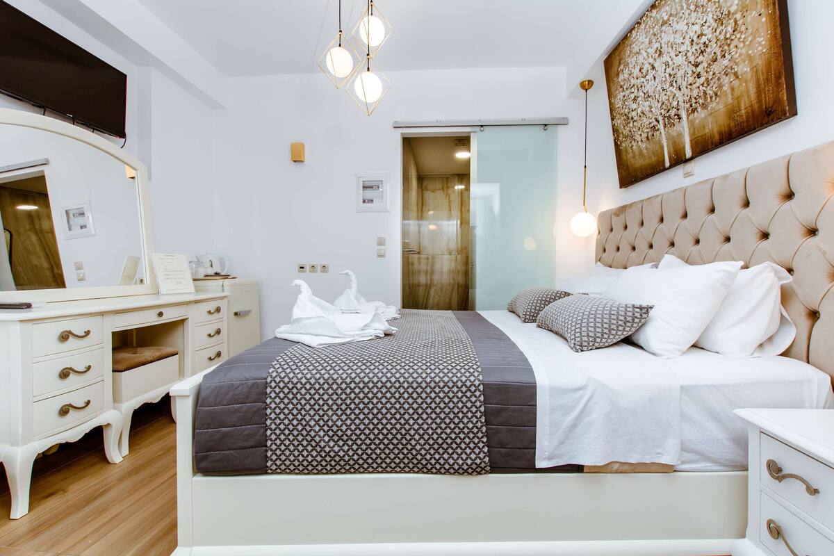 A modern bedroom with a large bed, a vanity with a mirror, and a painting on the wall.