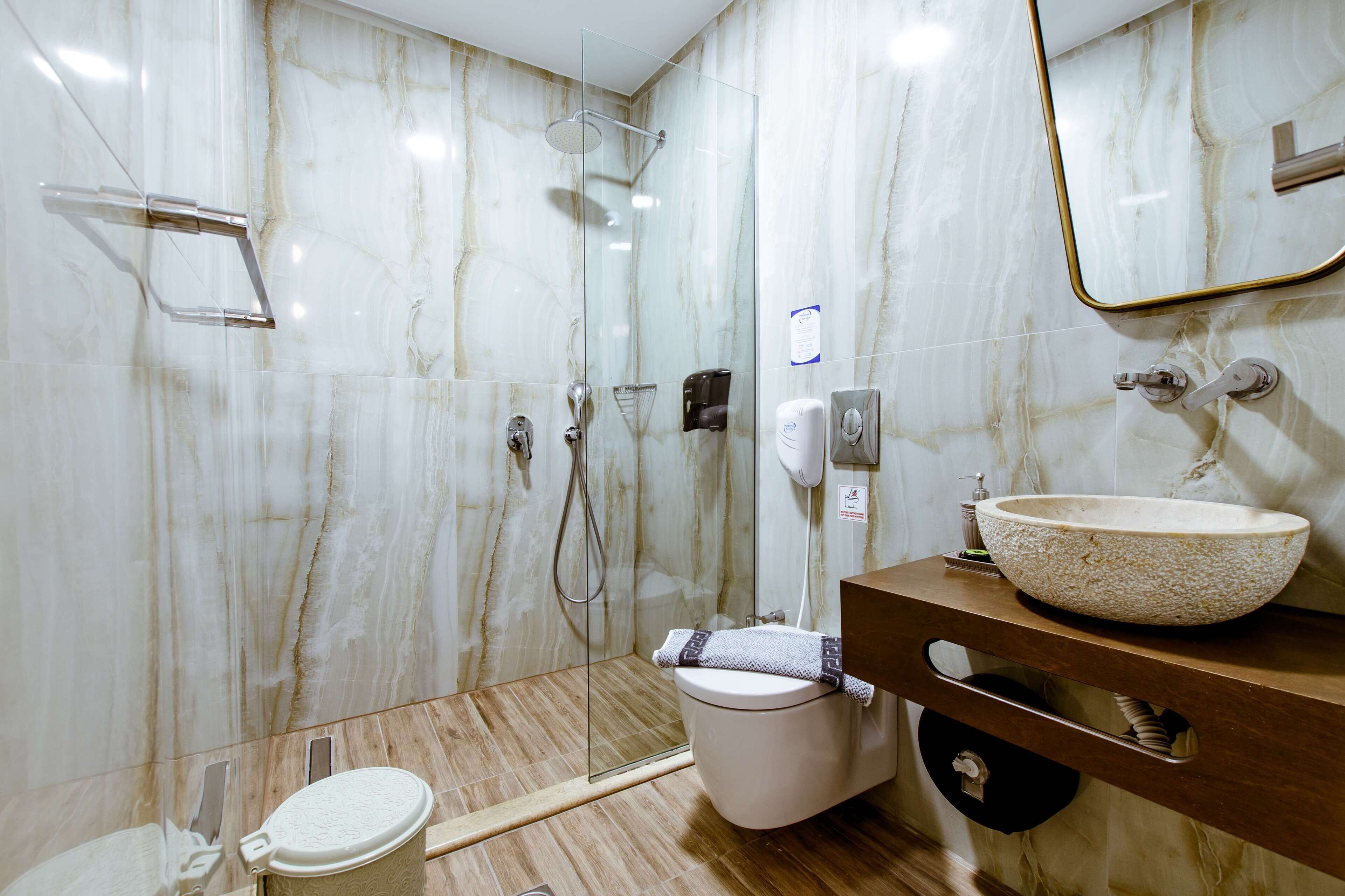 Un baño moderno con ducha de vidrio, pared de mármol, tocador de madera y un lavamanos grande.
